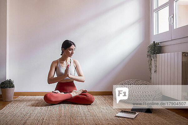 Young woman learning lotus position through tablet PC at home