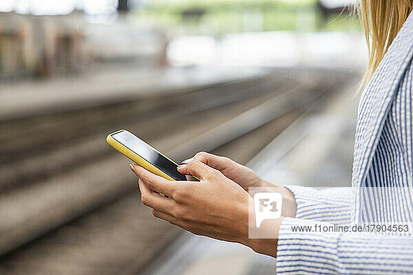 Hands of businesswoman using smart phone at railroad station