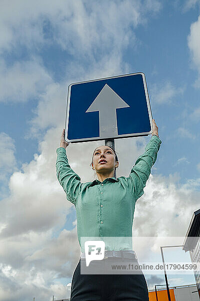 Businesswoman with arms raised holding arrow sign board under cloudy sky