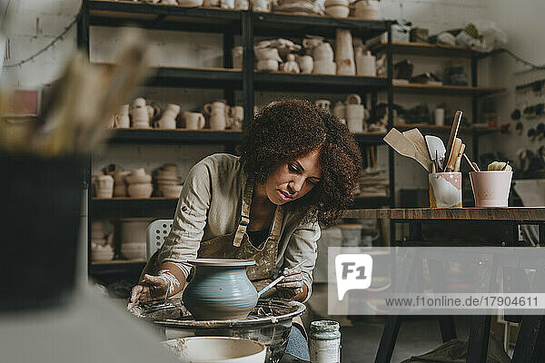 Young potter painting pot on pottery wheel at workshop