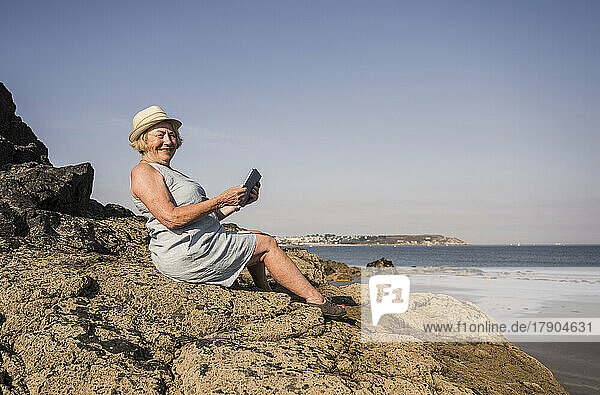 Happy woman with tablet PC sitting on rock at beach