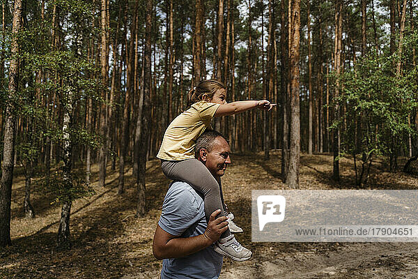Mature man carrying girl on shoulders and walking in forest