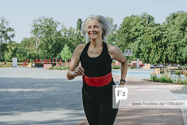 Glückliche reife Frau mit Hosenbund joggt im Park
