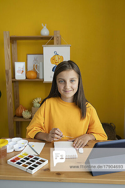Lächelndes Mädchen mit Skizzenblock am Tisch sitzend