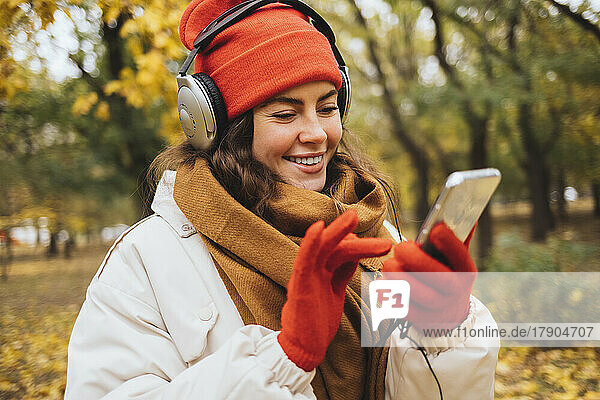 Smiling woman listening to music through headphones using smart phone at park