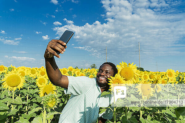 Happy man with sunflower taking selfie through mobile phone in field