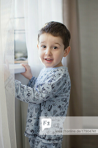 Cute boy standing by window at home