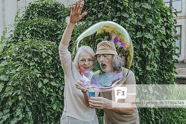 Glückliche reife Frau genießt es  wenn ein älterer Mann im Park Seifenblasen macht