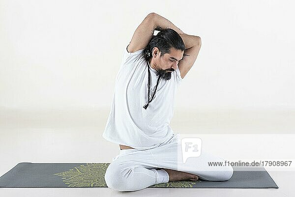 Ein weiß gekleideter Mann macht Yoga auf einer Matte vor weißem Hintergrund. bharadvajasana Yoga-Pose. Studioaufnahme