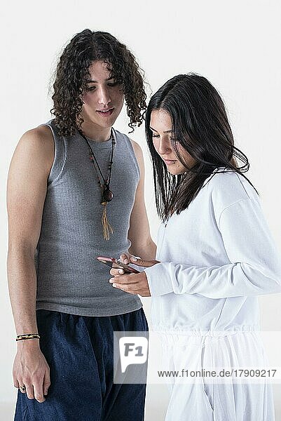 Porträt eines jungen Paares in Yogakleidung mit Blick auf ein Smartphone vor weißem Hintergrund. Studioaufnahme