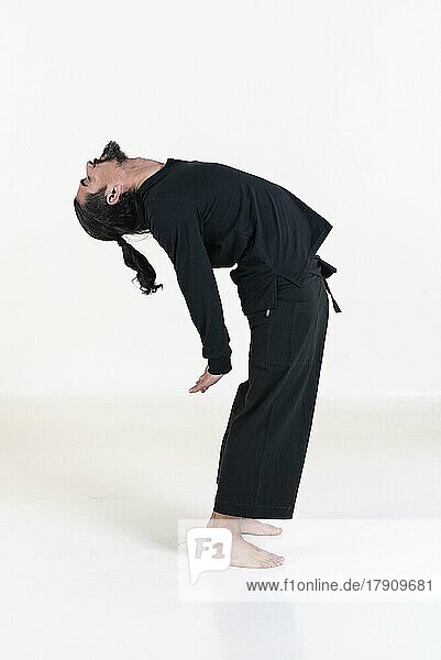 Ein Mann in schwarz gekleidet macht Yoga über weißem Hintergrund. Suryanamaskar Yoga-Pose. Studioaufnahme