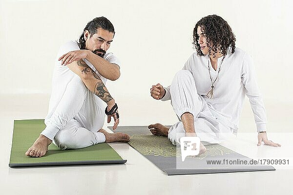 Ein Yogalehrer unterrichtet einen jungen Mann in Yoga. Beide sind mit weißer Yogakleidung bekleidet. Vorderansicht