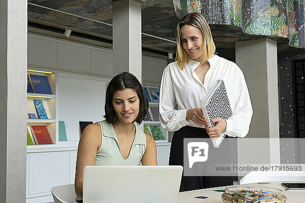 Mittelaufnahme einer lateinamerikanischen Innenarchitektin und ihrer Assistentin  die auf einen Laptop-Bildschirm schauen