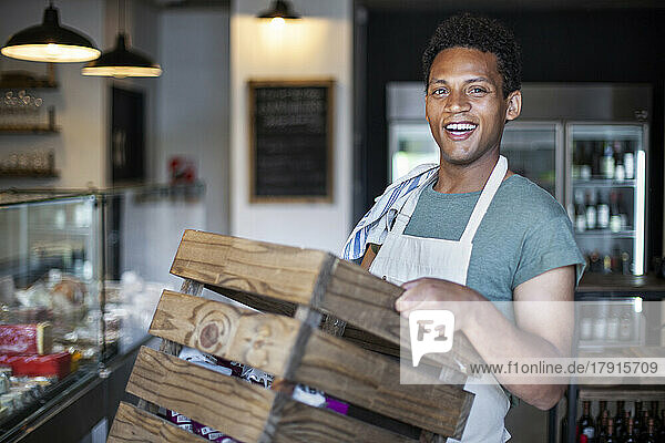 Young Latin American grocery store worker carrying wooden crate