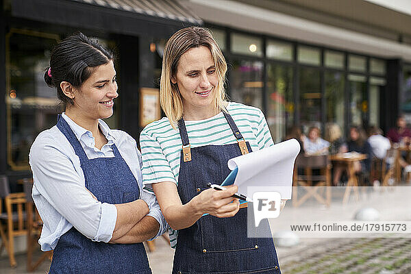 Mid-shot von zwei Unternehmerinnen  die vor ihrem Restaurant eine Liste prüfen