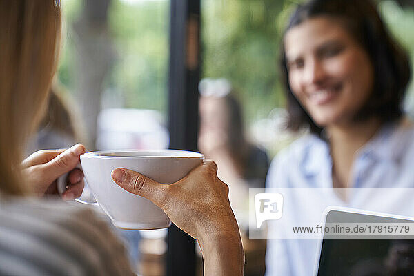 Nahaufnahme von hinten einer Frau  die eine Tasse Kaffee in der Hand hält und mit einem Freund spricht