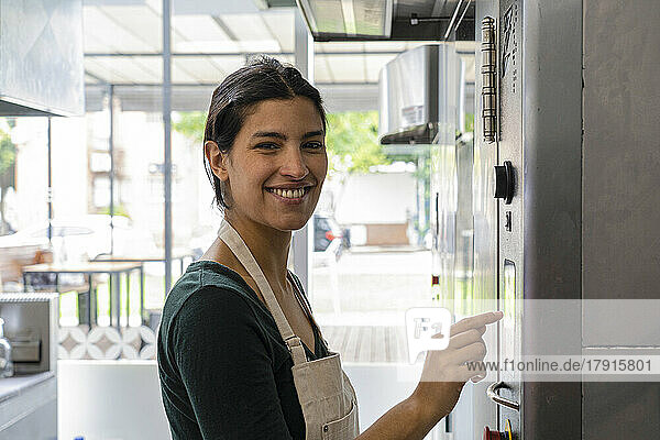 Mittlere Einstellung einer lateinamerikanischen Bäckereibesitzerin  die in die Kamera schaut  während sie den Timer für den Ofen einstellt