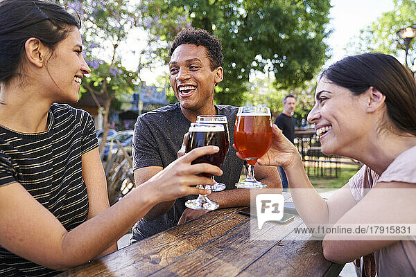 Eine Gruppe glücklicher Freunde erhebt ihre Biergläser zum Feiern in einer trendigen Kneipe im Freien