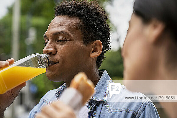 Seitenansicht eines afroamerikanischen Mannes  der Orangensaft trinkt  und seiner lateinamerikanischen Freundin  die ein Sandwich isst
