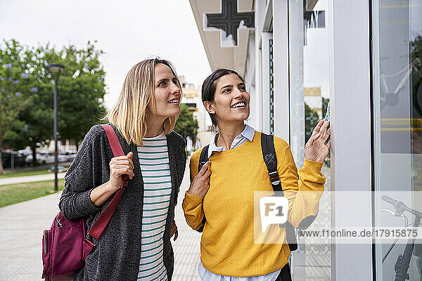 Photo of two female friends looking at shop windows and having a good time together