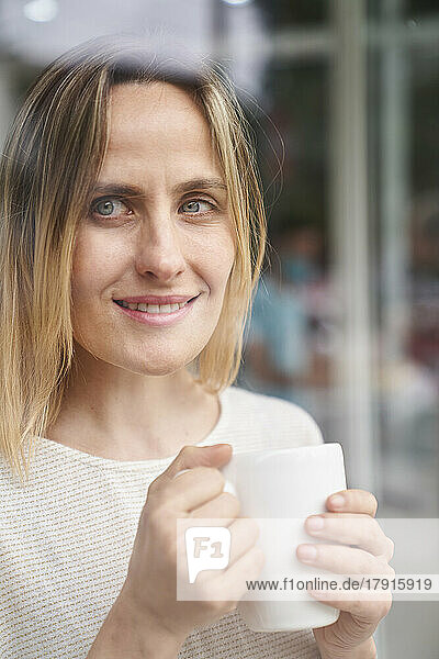 Porträt einer Frau  die eine Kaffeetasse hält und durch ein Fenster schaut