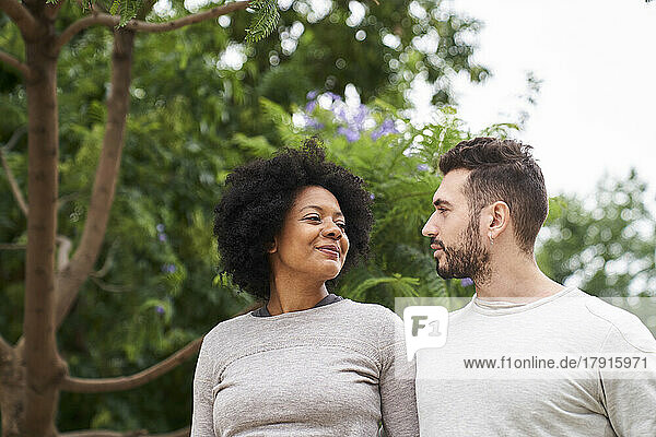 Porträt einer afroamerikanischen Frau und eines kaukasischen Mannes  die sich gegenseitig anschauen und sich im Freien amüsieren