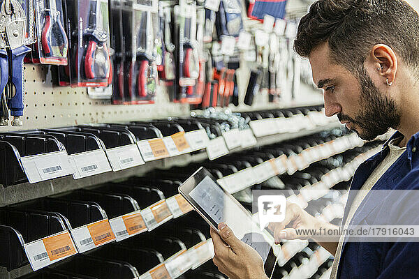 Male hardware shop worker taking inventory on digital tablet