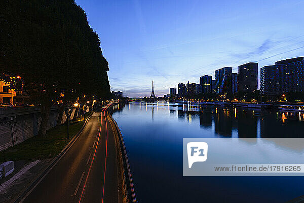 Blick entlang der Seine auf den Eiffelturm  die Uferpromenade und die Stadt in der Abenddämmerung  Spiegelungen auf dem Wasser.