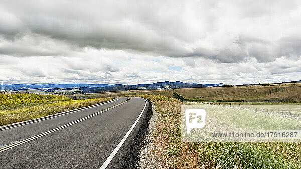 A blacktop road through a flat landscape with undulating hills  farmland and rolling hills beyond.