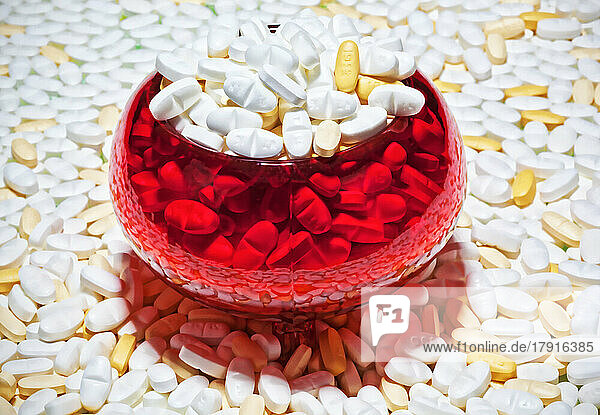 Pillen  Kapseln  weiß und braun  ausgebreitet und in einer roten Glasschale.