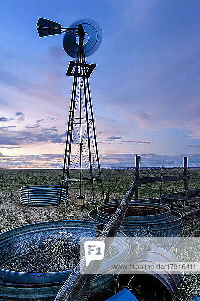 Eine sich drehende Windmühle mit Metallrad und Windturm  unscharfe Bewegung  bei Sonnenuntergang in der Prärie oder den Hochebenen von Colorado.