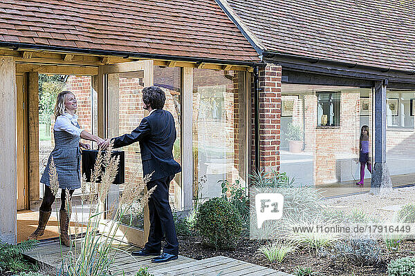 Ein Mann und eine Frau übergeben eine Aktentasche an der Tür eines umgebauten Scheunenhauses.