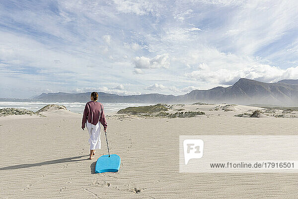 South Africa  Hermanus  Teenage girl (16-17) walking with body board on sand dunes in Walker Bay Nature Reserve