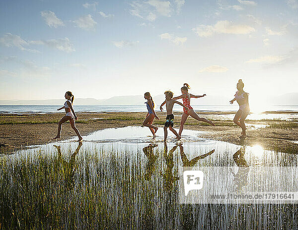 Group of children (10-11  12-13  14-15) walking on stepping stones in lake at sunrise