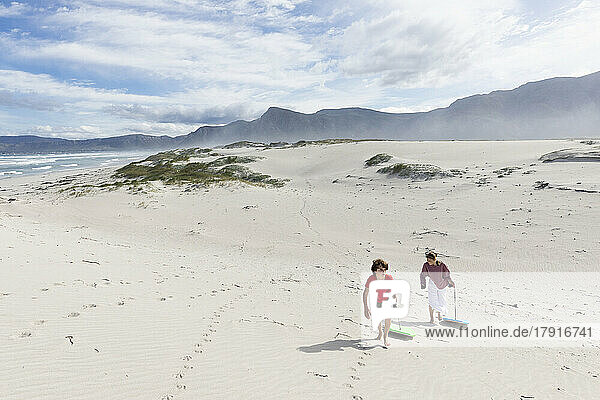 South Africa  Hermanus  Siblings (8-9  16-17) with body boards on sand dunes in Walker Bay Nature Reserve