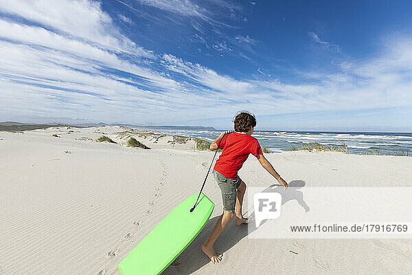 South Africa  Western Cape  Hermanus  Boy (8-9) preparing to surf down sand dunes in Walker Bay Nature Reserve