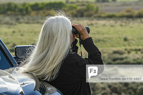 Rear view of woman looking through binoculars at car