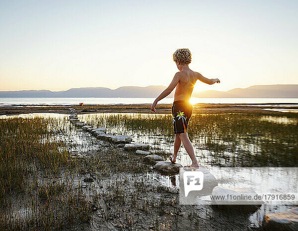 Rear view of boy (10-11) walking on stepping stones in lake at sunrise