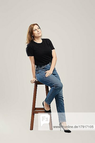 Junge Frau in schwarzem T-Shirt und Jeans  die nachdenkt und zu einem grauen Hintergrund aufschaut