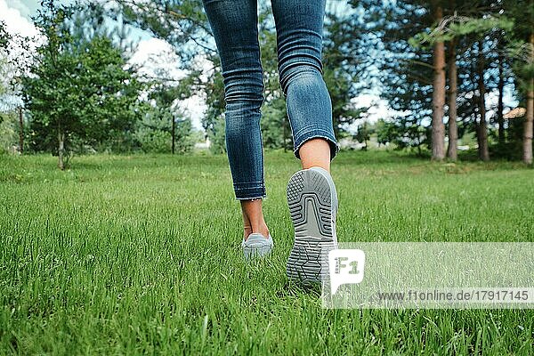 Rückansicht von weiblichen Beinen in Jeans und Turnschuhen  die auf Gras laufen