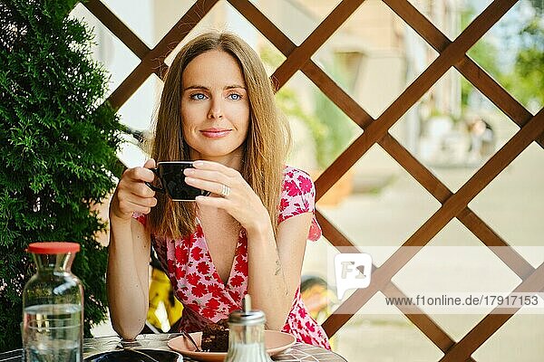 Junge Frau hält eine Tasse Kaffee in der Hand  sitzt auf der Terrasse und genießt die Freiheit