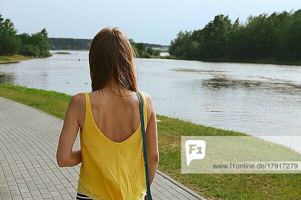 Rückansicht des Spaziergangs entlang des Flusses hübsches Mädchen mit Wind im Haar