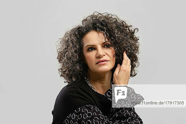 Senior woman touching lush curly hair in studio over grey background