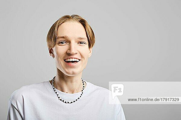 Closeup portrait of laughing young man in white t-shirt over grey studio background