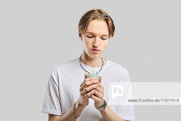 Young man holds candle in hand over grey studio background
