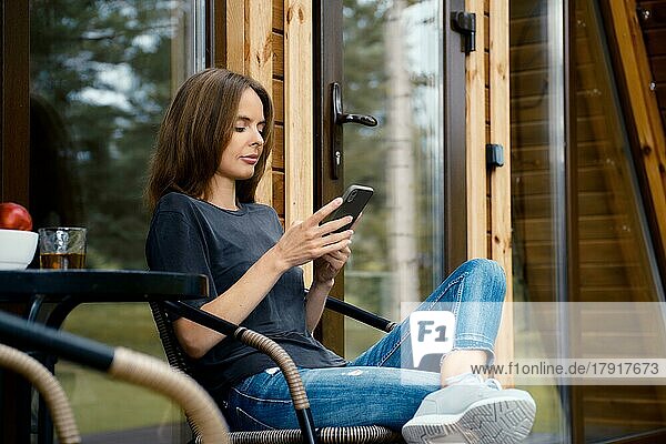Frau sitzt mit Mobiltelefon auf der Terrasse und liest Nachrichten