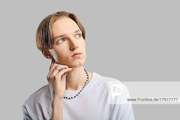 Closeup portrait of pensive young man in white t-shirt over grey studio background