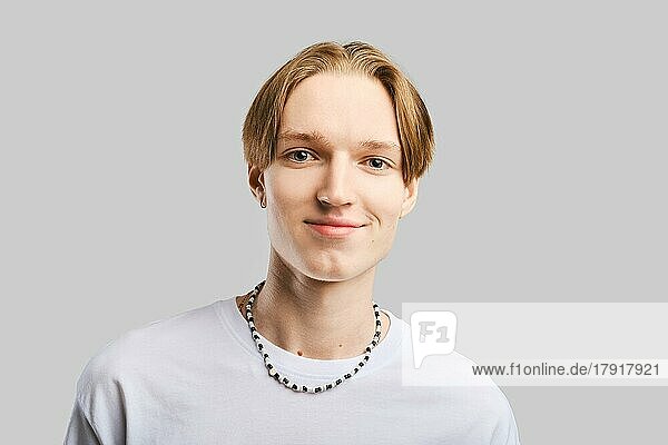Closeup-Porträt eines lächelnden jungen Mannes im weißen T-Shirt vor grauem Studiohintergrund