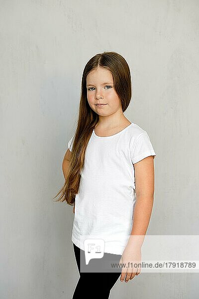 Niedliches kleines Kind mit langen Haaren in weißem T-Shirt und schwarzer Jogginghose posiert