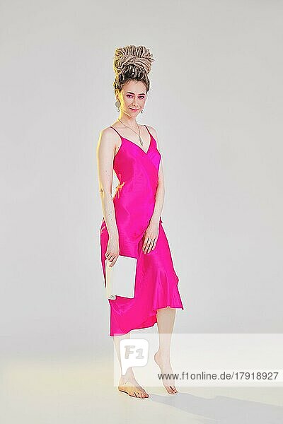 Young barefoot woman in pink silk strap dress holds open book in hand